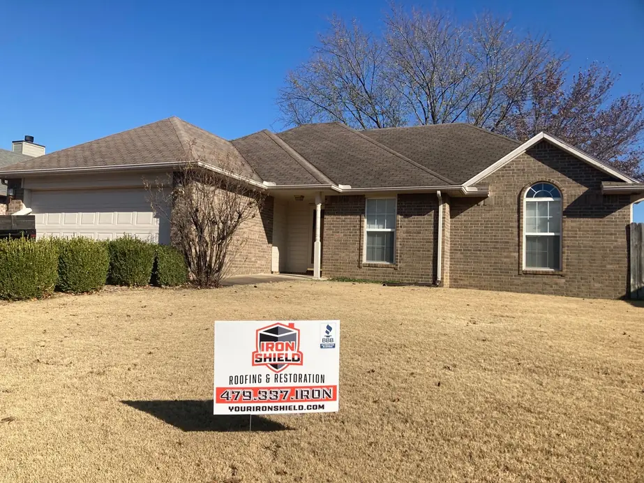 A single-storey brick home with a finished roof and an Iron Shield sign on the lawn