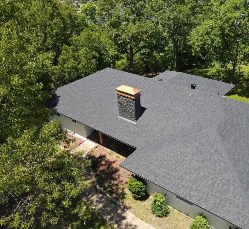 A finished charcoal shingle roof with a copper-capped stone chimney, seen from above
