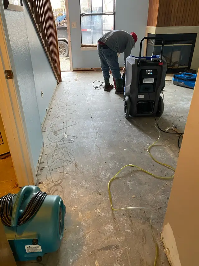 Flooring lifted to the slab with a dehumidifier and an air mover running during a water damage job
