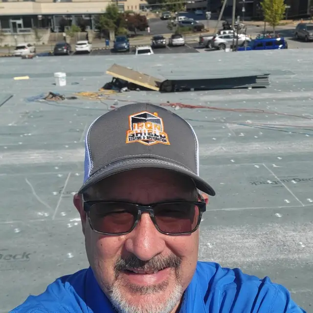 A team member in an Iron Shield cap on a commercial flat roof during tear-off and re-deck